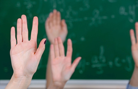 Raised hands on blackboard background in classの写真素材