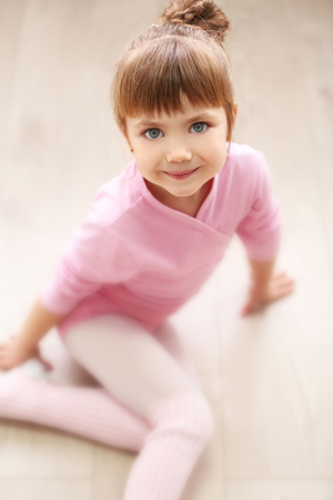 Little cute girl in pink leotard sitting on floor at dance studioの写真素材