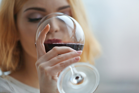 Young woman with glass of red wine on light blurred backgroundの写真素材