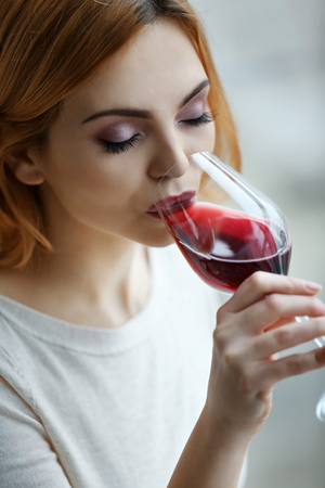 Young woman with glass of red wine on light blurred backgroundの写真素材