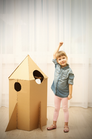 Little cute girl playing with cardboard space rocket in roomの写真素材