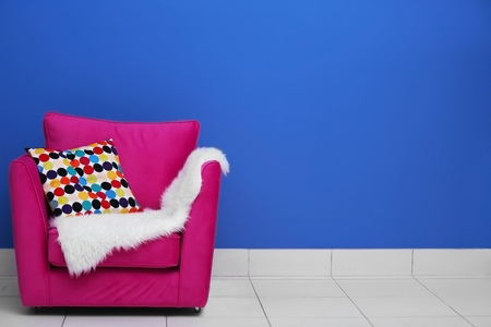 Comfortable armchair with pillow and blanket against blue wall backgroundの写真素材