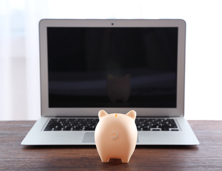 Piggy bank with laptop on wooden table indoorsの写真素材