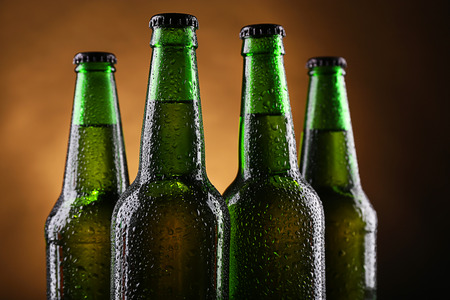 Four green glass bottles of beer on dark lighted background, close upの写真素材