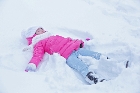 Little girl with winter clothes lying on the snow outdoorの写真素材