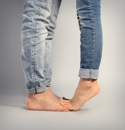 Young woman standing on the boyfriend's feet over grey background