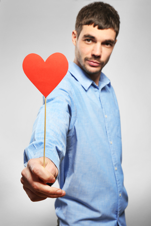 Young man holding red paper heart on grey backgroundの写真素材