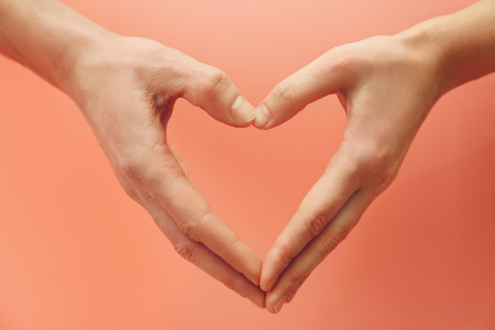 Male and female hands making heart with fingers on pink backgroundの写真素材