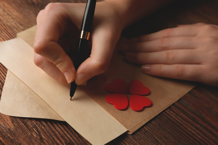 Female hands signing gift card for Valentine's Day on wooden backgroundの写真素材