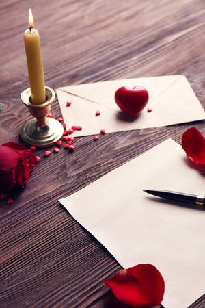 Gift card for Valentine's Day with red rose, pen and candle on wooden backgroundの写真素材