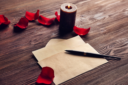 Gift card for Valentine's Day with pen, red petals and candle on wooden backgroundの写真素材
