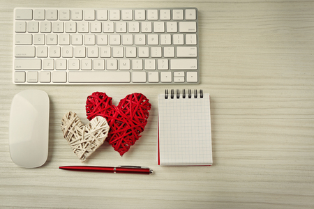 Computer peripherals with wicker hearts, pen and notebook on light wooden tableの写真素材