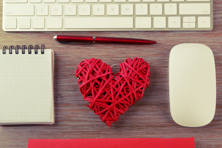 Computer peripherals with red wicker heart, pen and notebook on wooden tableの写真素材