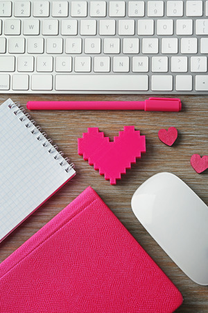 Computer peripherals with pink hearts, pen and notebooks on wooden tableの写真素材