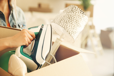 Woman putting iron in cardboard box for moving into new houseの写真素材