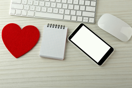 Computer peripherals with red heart, notebook and mobile phone on light wooden tableの写真素材