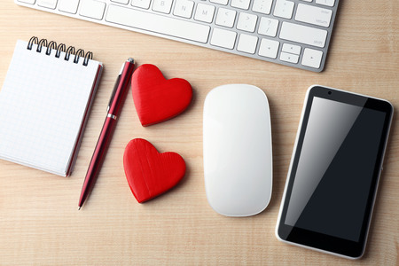 Computer peripherals with red hearts, notebook and mobile phone on light wooden tableの写真素材