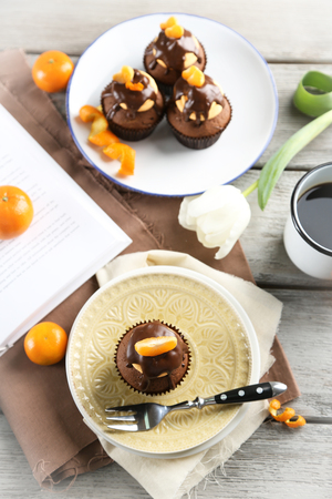 Tasty cupcakes with slice of mandarin and chocolate on a plate over light wooden backgroundの写真素材