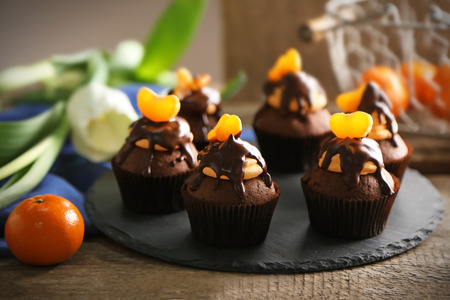 Tasty cupcakes with slice of mandarin and chocolate on slate plate over wooden backgroundの写真素材
