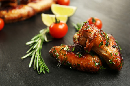 Baked chicken wings with tomatoes and rosemary on slate plateの写真素材