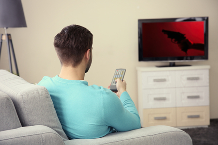 Young handsome man watching TV on a sofa at homeの写真素材