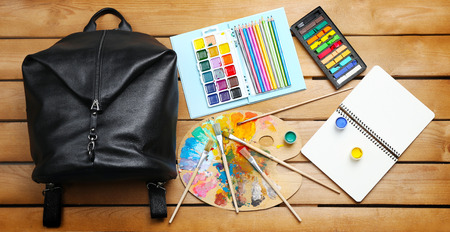 School set with backpack, shoes and supplies on wooden background