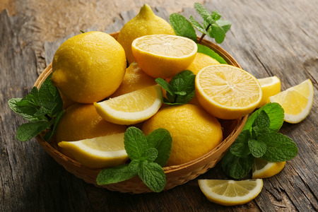 Fresh lemons with green leaves in bowl on wooden backgroundの写真素材