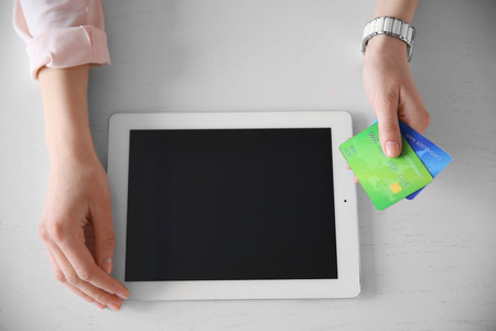Female hands holding digital tablet and credit card on white table, closeup
