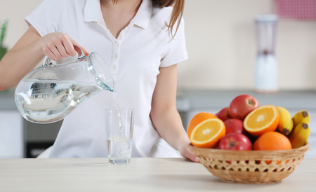 Young woman pouring water from jug into glass in the kitchenの写真素材