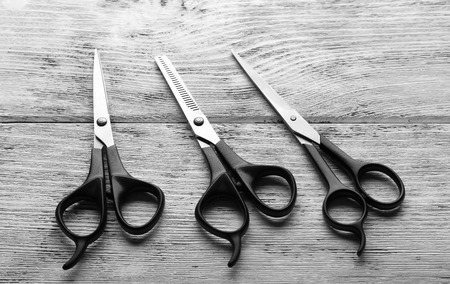 Three professional metal scissors with black handles lying beside each other on the wooden table, close upの写真素材