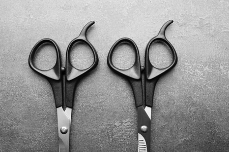 Professional scissors with black handles on a dark grey surface, top view