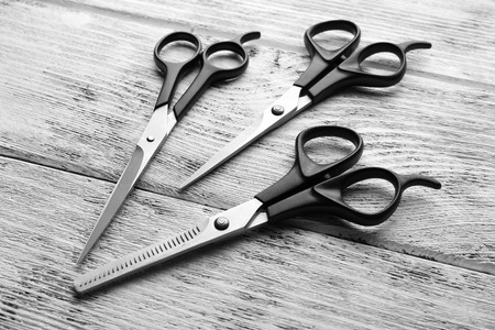 Three professional metal scissors with black handles lying beside each other on the wooden table, close upの写真素材