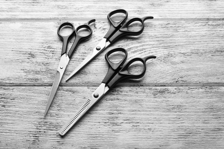 Three professional metal scissors with black handles lying beside each other on the wooden table, close upの写真素材