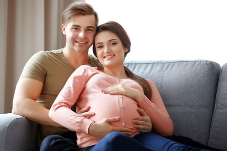 Pregnant woman with husband sitting on sofa in the room