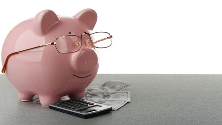 Pink piggy bank with dollar banknotes, glasses and calculator on white backgroundの写真素材