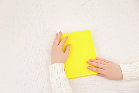 Female hands holding a yellow book cover  on white desk, top viewの写真素材