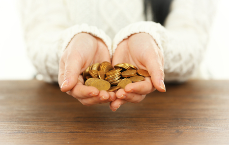 Young woman in a white knitted sweater holding a heap of  coins in her hands above  wooden table, close upの写真素材