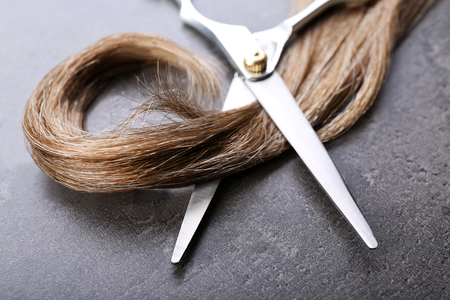 Hairdresser's scissors with strand of brown hair on grey backgroundの写真素材