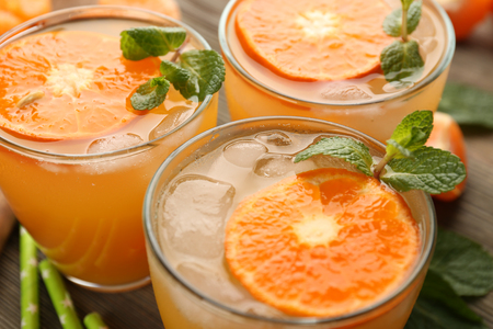 Delicious tangerine cocktails with sliced mandarins, ice, garnished with a mint, served on a wooden table, close upの写真素材