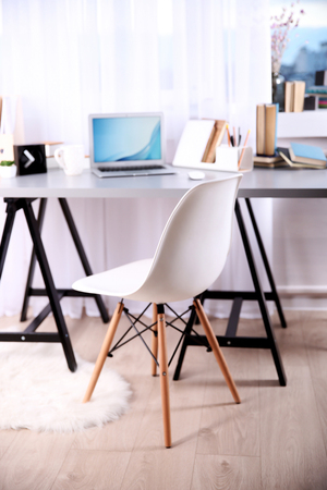 Workplace with laptop, table and chair beside the windowの写真素材