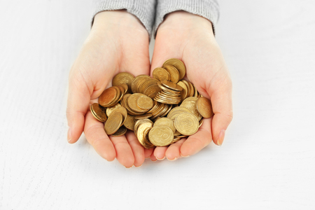 Young woman in a grey shirt  holding a heap of coins in her hands above white wooden surface, close upの写真素材