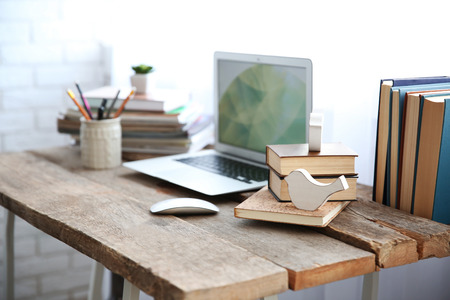 Workplace with laptop, table and books beside the windowの写真素材