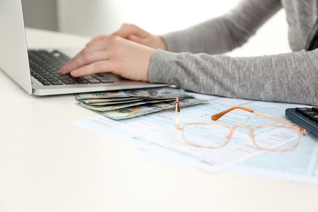 Woman set aside calculator, money, paper, her glasses and using computer on the white wooden table, close upの写真素材