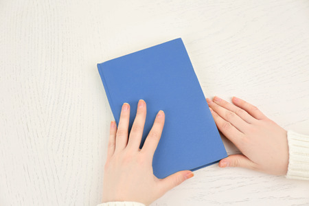 Female hands holding a light-blue book cover  on white desk, top viewの写真素材