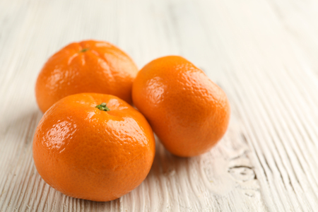 Three fresh delicious unpeeled tangerines on the white wooden table, close upの写真素材