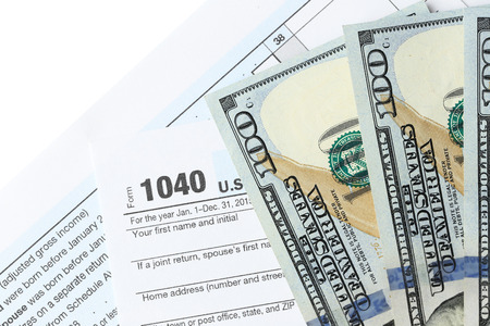 1040 Individual Income Tax Return Form with one hundred dollar bills on white background, close up