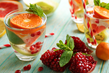 Refreshing cocktails with ice, mint, pomegranate seeds and slices of fruits on blue wooden backgroundの写真素材