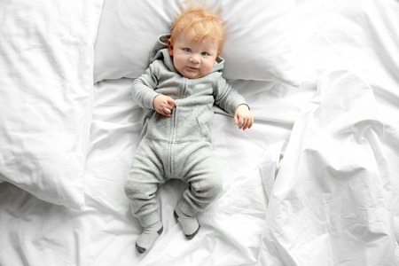 Little baby boy in grey pajamas lying on the bedの写真素材