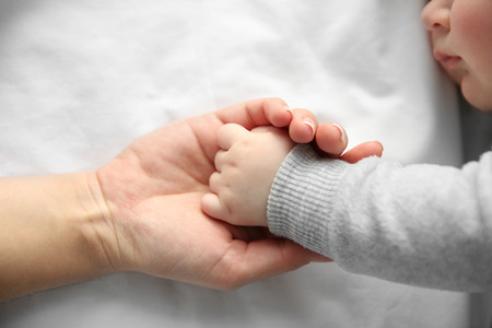 Hands of mother and her little baby boy on the bed, close upの写真素材