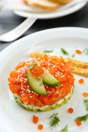Fresh tartar with salmon, avocado, cucumber and red caviar on white plate, close upの写真素材